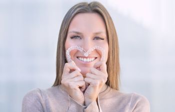 Woman with a perfect smile holding clear aligners bent n a shape of heart.