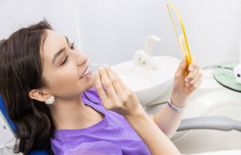 Young woman with clear aligner looking at her teeth in a mirror during an orthodontic appointment.